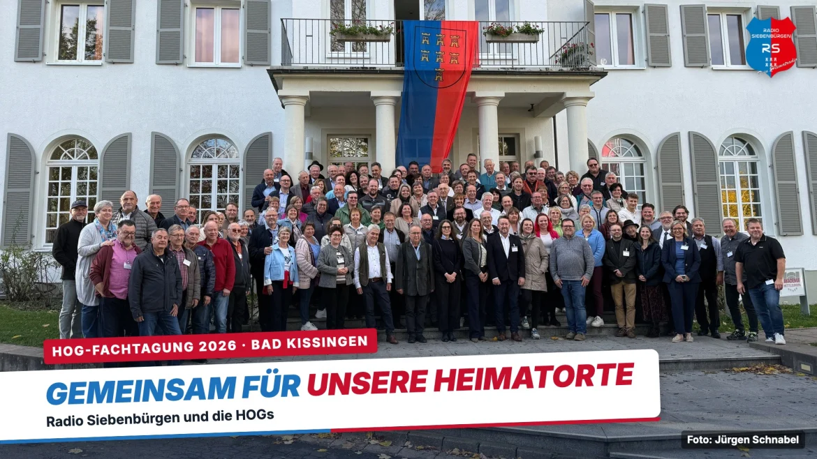 Gruppenbild der Teilnehmerinnen und Teilnehmer der HOG-Fachtagung 2026 vor dem Heiligenhof in Bad Kissingen, über dem Eingang die Fahne der Siebenbürger Sachsen, mit Bauchbinde „Gemeinsam für unsere Heimatorte – Radio Siebenbürgen und die HOGs“